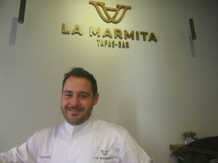 El cocinero Enrique Hidalgo delante del logotipo de la firma. Foto: Cosasdecome